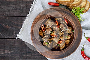 Pieces of fried pork with chilli in a clay bowl on a dark wooden background.