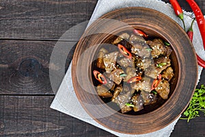 Pieces of fried pork with chilli in a clay bowl on a dark wooden background.