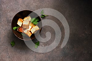 Pieces of fried tofu cheese in a bowl on a dark rustic background. Overhead view, copy space