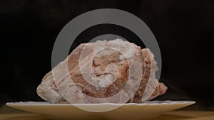 Pieces of frozen rotating meat on a black background, from which blows frosty freshness and cold, smoke, close-up, slow