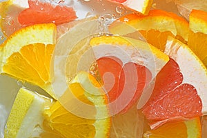 Pieces of grapefruit, orange fruit and honey pomelo in liquid with bubbles. Slices of grapefruit, orange fruit and honey