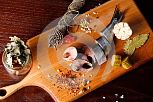 pieces of herring on a cutting Board, next to pepper, garlic, tomatoes on a branch ,parsley, pickled cucumber.