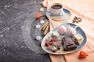 A pieces of homemade chocolate with coconut candies and a cup of coffee on a black concrete background. side view, copy space
