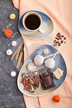 A pieces of homemade chocolate with coconut candies and a cup of coffee on a black concrete background. top view, close up
