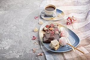 A pieces of homemade chocolate with coconut candies and a cup of coffee on a gray concrete background. side view, copy space