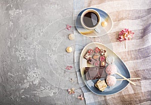 A pieces of homemade chocolate with coconut candies and a cup of coffee on a gray concrete background. top view, copy space