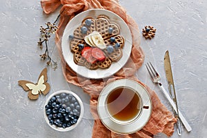 Pieces of homemade waffle cake with banana and blueberries on the plates on gray background.