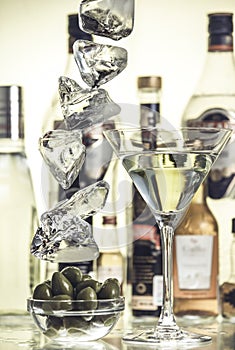 Pieces of ice, glass bowl with green olives and a glass of martini