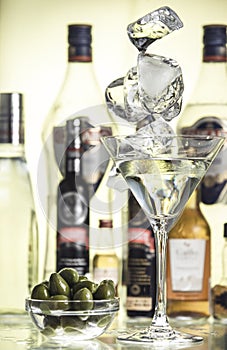 Pieces of ice, glass bowl with green olives and a glass of martini