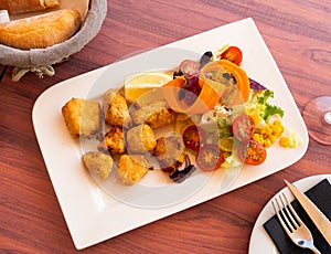 Pieces of marinated dogfish with sliced vegetables on wooden table