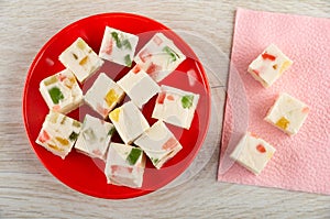 Pieces of marshmallow with marmalade in red saucer, marshmallow on paper napkin on table. Top view