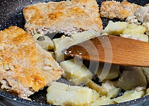 Pieces of meat pie and potatoes in frying pan