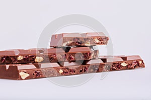Pieces of milk chocolate bars with hazelnuts and cranberries on white background.