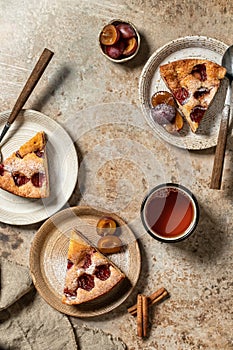 Pieces of The New York Times Plum Cake pie sprinkled with powdered sugar for tea on brown textured background, autumn