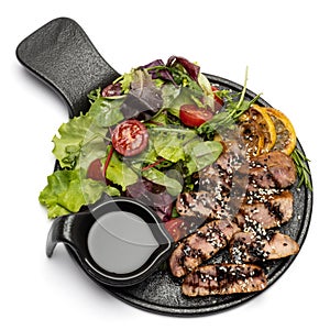pieces of Organic grilled Tuna Steak on black ceramic serving dish with salad isolated
