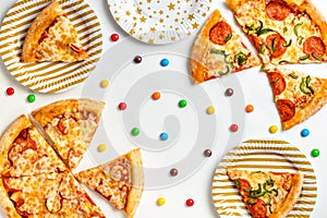 Pieces of pizza and colored sweets on a white background. Birthday with junk food. Children`s party. Top view with copy