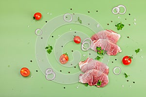 Pieces of pork meat with parsley, purple onion rings and tomato, raw fresh steaks concept