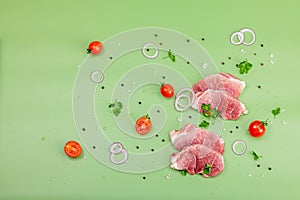 Pieces of pork meat with parsley, purple onion rings and tomato, raw fresh steaks concept