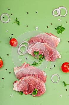 Pieces of pork meat with parsley, purple onion rings and tomato, raw fresh steaks concept