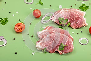 Pieces of pork meat with parsley, purple onion rings and tomato, raw fresh steaks concept