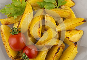 Pieces of potato baked in a country style served with small ripe tomatoes and parsley. Baked potato with vegetables, close-up top