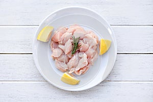 Pieces of raw chicken meat with rosemary and lemon / fresh raw cut chicken fillet on white plate background