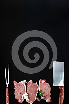 Pieces of raw roast beef meat with ingredients, meat knife and meat fork on dark background
