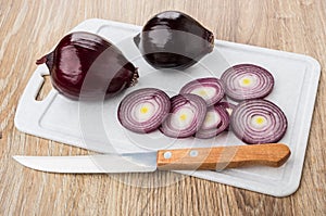 Pieces of red onion and kitchen knife on cutting board