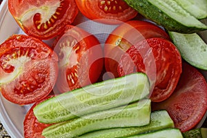 Pieces of red tomatoes and fresh cucumbers on a white plastic plate