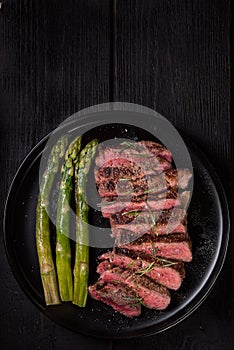 Pieces of Ribeye steak with asparagus on a black plate. View from above.