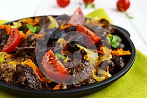 Pieces of roast duck, goose meat, liver, heart with vegetables onion, carrot, tomato, with spices on a round cast-iron frying