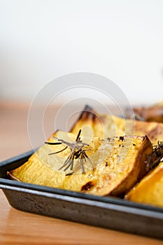 Pieces of roasted butternut squash in a baking sheet pan with fresh thyme and sage herbs in natural light.