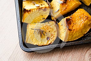 Pieces of roasted butternut squash in a baking sheet pan with fresh thyme and sage herbs in natural light.