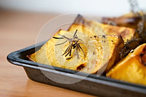 Pieces of roasted butternut squash in a baking sheet pan with fresh thyme and sage herbs in natural light.