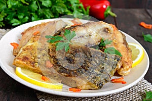 Pieces of roasted carp with lemon and greens on a plate