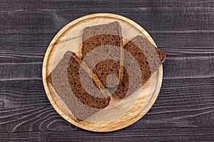 Pieces of rye flour black bread on a wooden serving plate and black rustic background