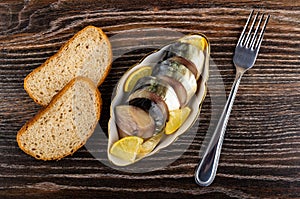 Smoked mackerel with lemon in bowl, bread, fork on table. Top view