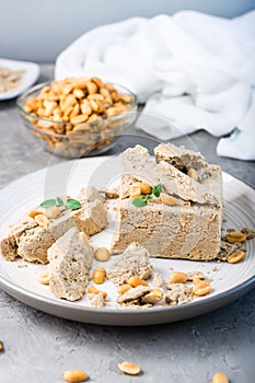 Pieces of sunflower and peanut halva and mint leaves on a plate and a bowl of nuts on the table. Caloric oriental delicacy.