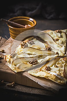 Pieces of a tarte flambee with pear, goat cheese, honey and walnuts on dark rustic wooden background