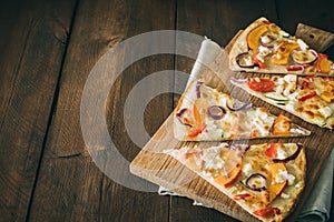 Pieces of tarte flambee with pumpkin, red onions and cheese on a rustic wooden table