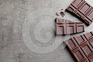 Pieces of tasty chocolate on grey background, flat lay.