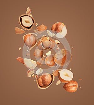 Pieces of tasty hazelnuts falling on brown background