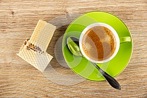 Pieces of wafer, black coffee in cup, spoon on saucer on wooden table. Top view