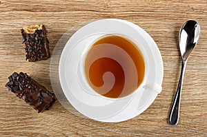 Pieces of wafer in chocolate, cup of tea on saucer, spoon on table. Top view