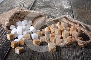 Pieces of white and brown sugar lie in bags on a wooden table. Different refined sugar cubes on wooden background