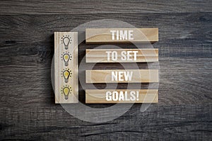 Pieces of wood, blocks with lightbulb icon and time to set new goals on wooden background