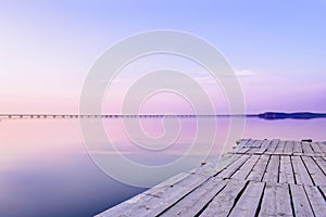 Pier on the background of the sea with a glossy surface, which reflects the pink-blue sky