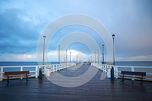 Pier on the Baltic Sea. Many birds on the sea and a wooden pier. There are many lanterns on the pier. A flock of birds over the se