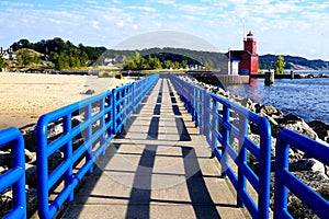 Pier with a bright blue fence in perspective. Big Red Lighthouse on the Lake Michigan
