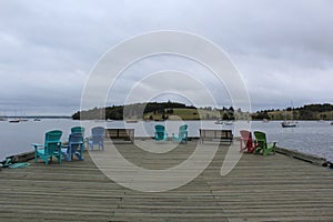A pier with colorful chairs in Lunenburg Nova Scotia looking out at the bay and sailboats